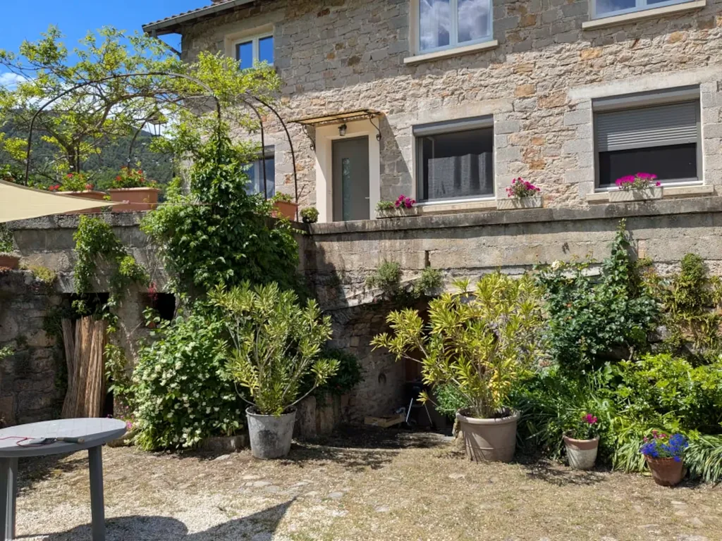 Façade en pierre et cour fleurie du gîte Au bord du Tarn
